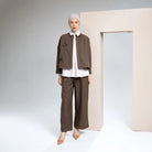 Person wearing a brown outer jacket by Hijabchic with a white shirt and beige hijab against a plain background