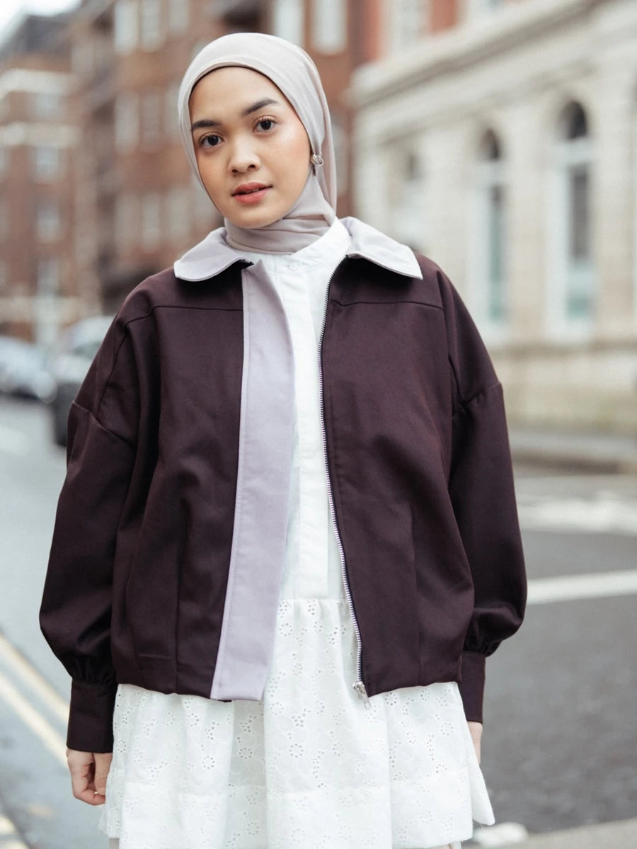 Woman wearing a brown jacket by Haidee Orlin over a white shirt and skirt on a city street.