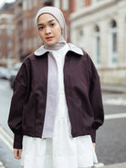 Woman wearing a brown jacket by Haidee Orlin over a white shirt and skirt on a city street.