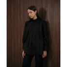 Woman wearing a black blouse by Kasa Heritage against a wooden paneled wall