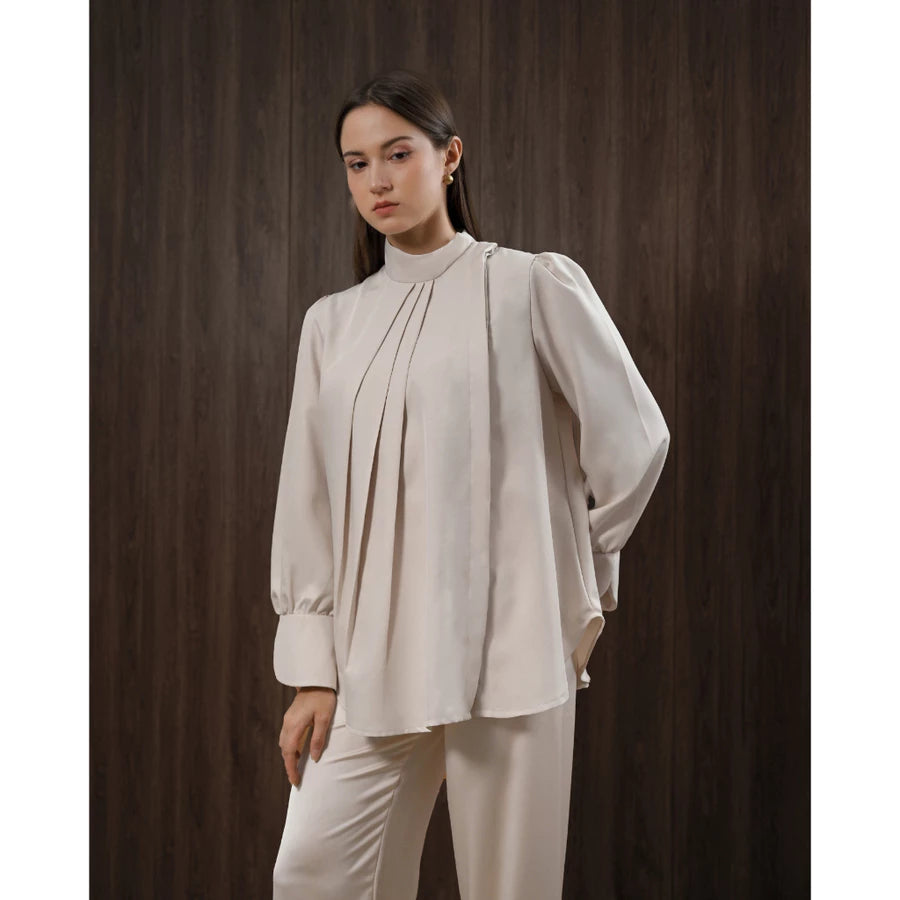 Woman wearing a beige blouse and pants by Kasa Heritage against a dark brown background