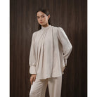 Woman wearing a beige blouse and pants by Kasa Heritage against a dark brown background
