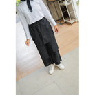 A person wearing a grey long-sleeve top and black wide-leg pants with an asymmetrical hem by Casa Elana, paired with white sneakers.