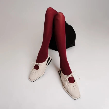 Ivory-colored flat shoes by Cekhas with red tights on a plain background