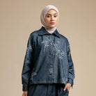 Woman wearing a blue denim jacket by Hijabchic with floral embroidery on a beige background