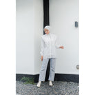 Woman wearing a white layered long-sleeve shirt by Casa Elana, light blue jeans, and a white hijab standing against a minimalist white wall.