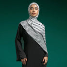 Woman wearing a black outfit with a white and black checkered hijab by Lozy Hijab against a green background