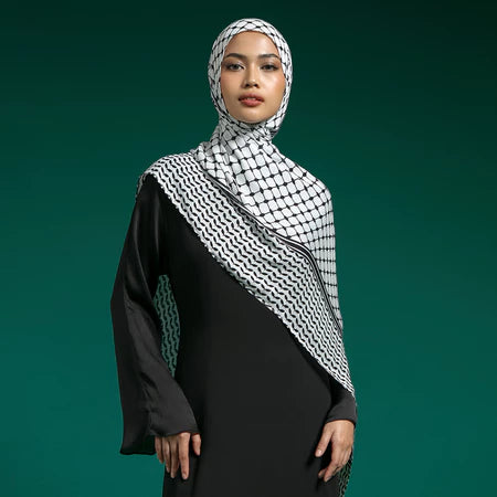 Woman wearing a black outfit with a white and black checkered hijab by Lozy Hijab against a green background
