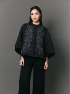 Woman wearing a black patterned outer with floral embriodery by Studio Tui against a gray background