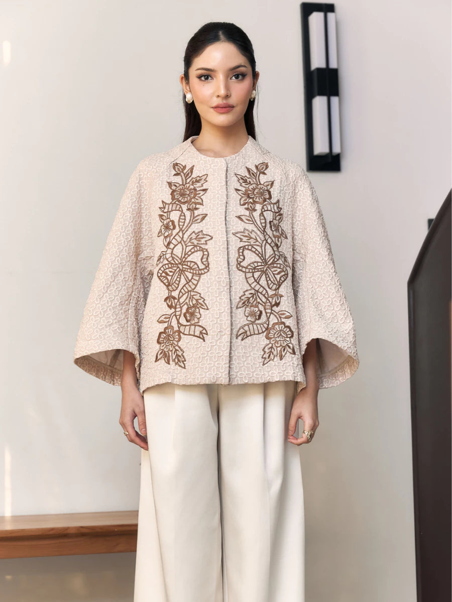 Woman wearing a beige embroidered outer by Studio Tui in an indoor setting.