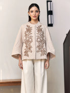 Woman wearing a beige embroidered outer by Studio Tui in an indoor setting.