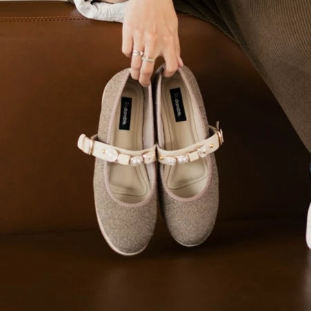 Pair of beige flat shoes with a decorative strap by Dianable on a brown surface