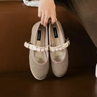 Pair of beige flat shoes with a decorative strap by Dianable on a brown surface