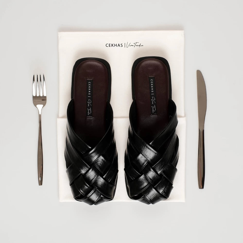 Black woven sandals by Cekhas on a white box with a fork and knife on a light gray background