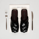 Black woven sandals by Cekhas on a white box with a fork and knife on a light gray background