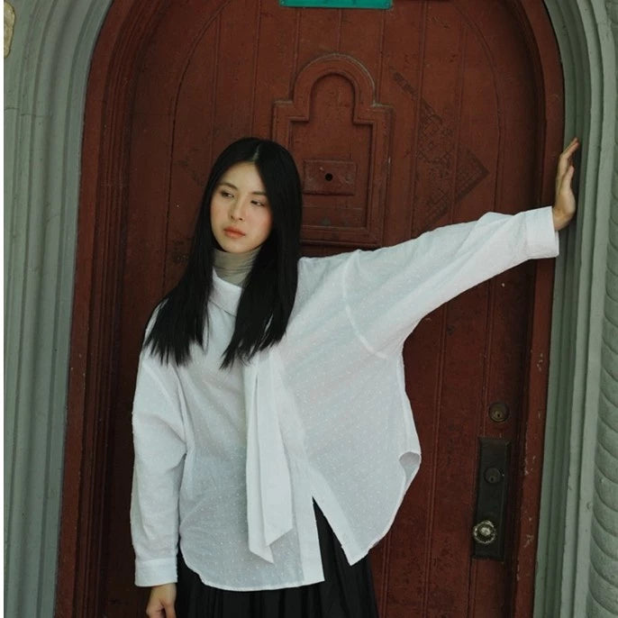 Woman in a white shirt by Yestoday standing in front of a wooden door