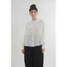 Person wearing a light-colored button-up shirt by Yestoday and dark pants on a white background