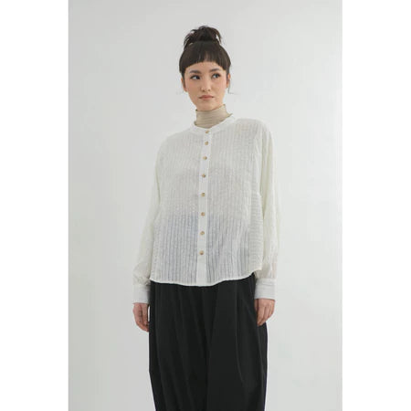 Person wearing a light-colored button-up shirt by Yestoday and dark pants on a white background