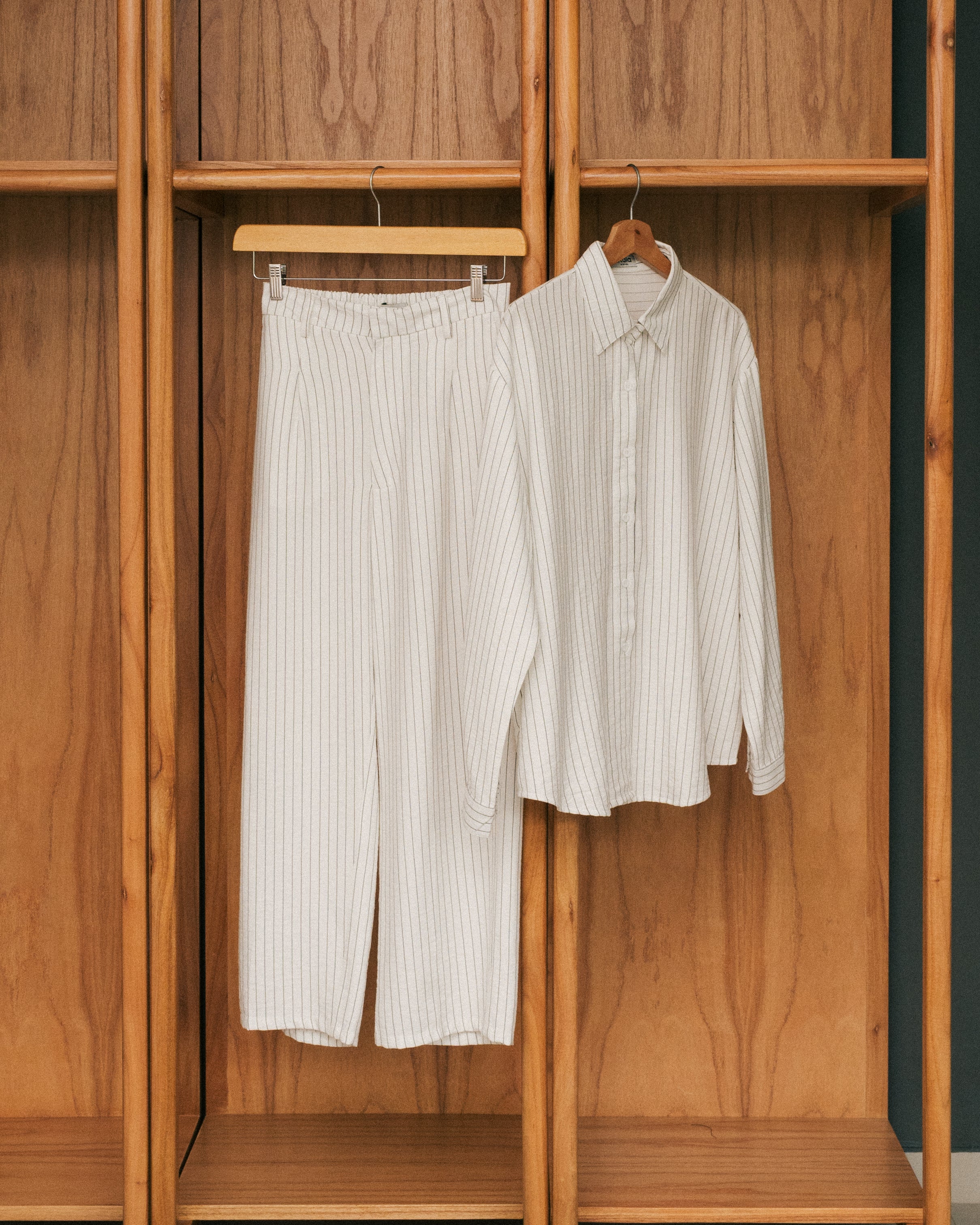 Broken white striped shirt and pants from Atala Scarves hanging on a wooden wardrobe.