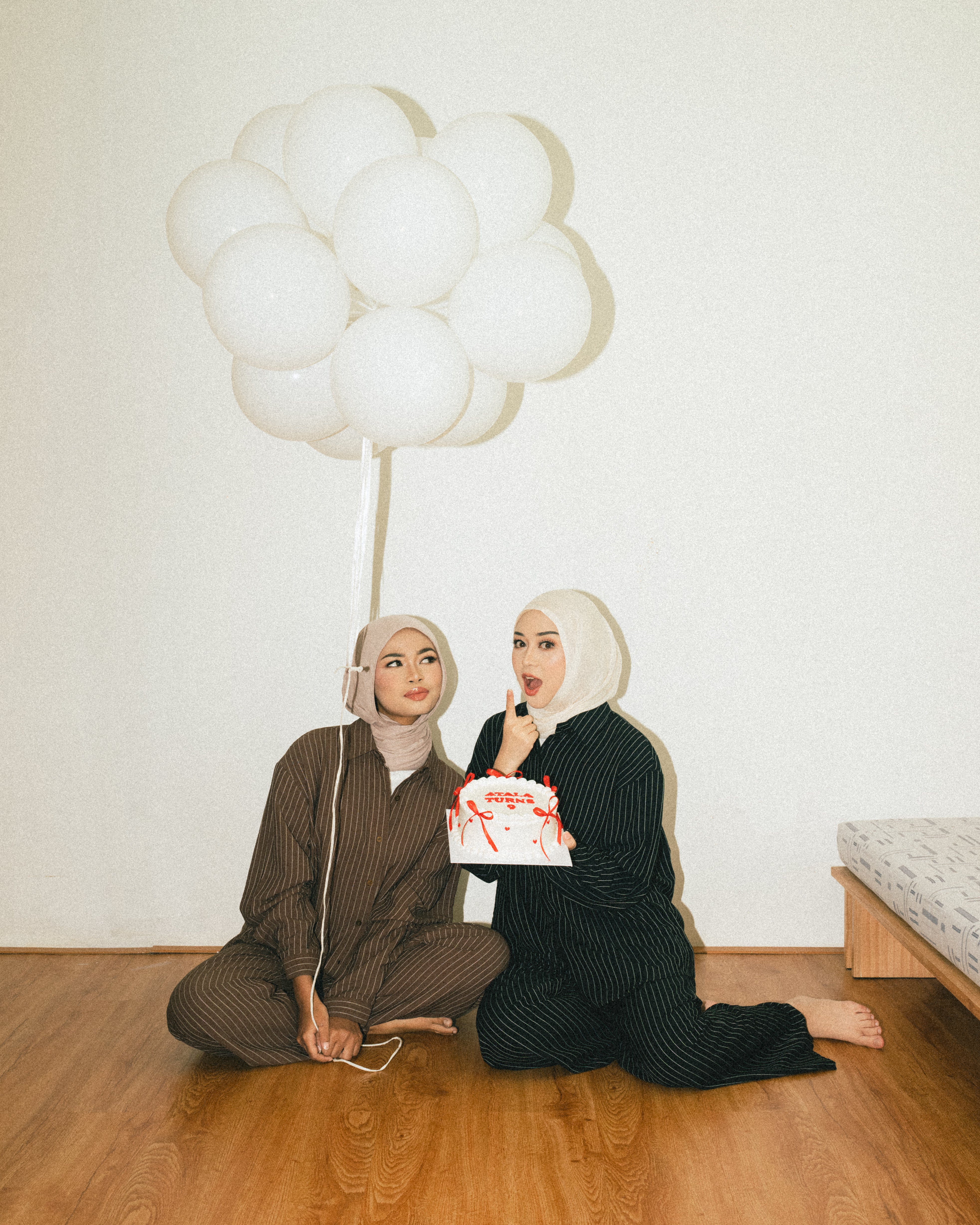 Two people sitting on the floor with balloons and a box, wearing linen outfit from Atala Scarves.