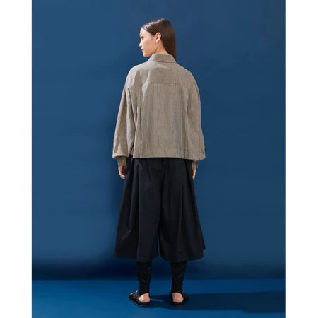 Person wearing a beige jacket and black wide pleated pants by Yestoday against a blue background