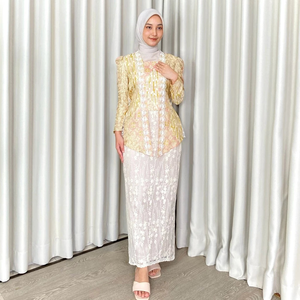 A woman wearing a traditional white skirt by Kartinis Label with floral patterns, standing in front of a curtain.