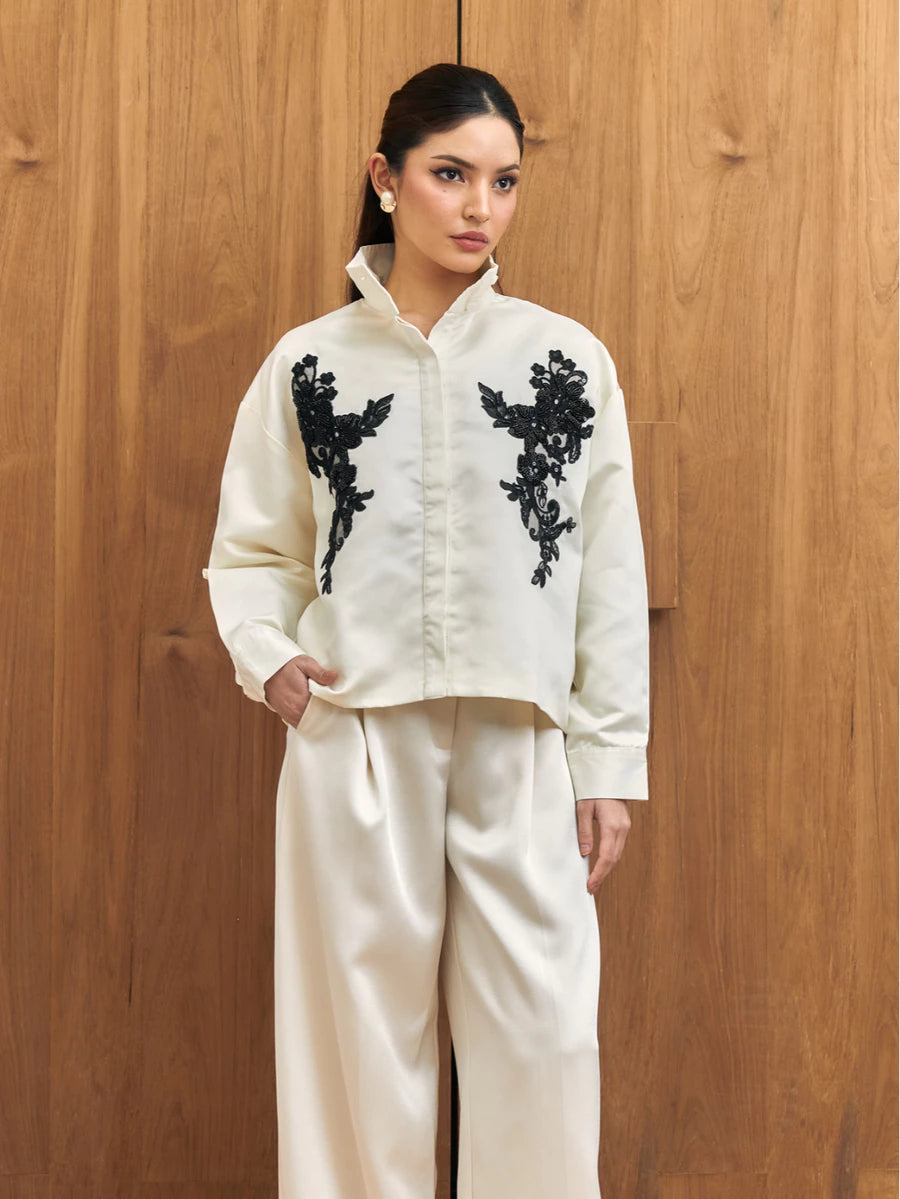 Woman wearing a white shirt with black floral embroidery by Studio Tui against a wooden background