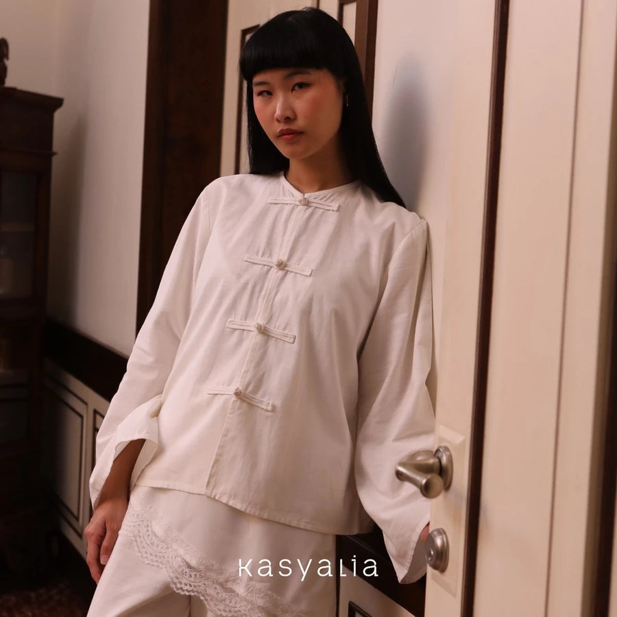 Woman wearing a white blouse by Kasyalia standing in a room with a door.