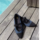 Pair of black and blue flatshoes by Tutu Toe on a wooden deck near a pool.