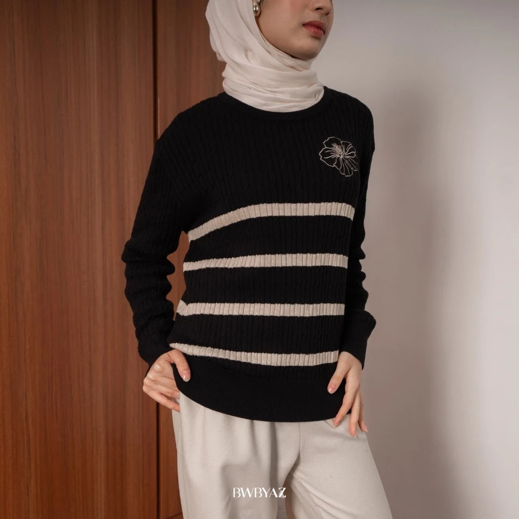 A person wearing a black and beige cable knit sweater with a round neckline, featuring horizontal stripes and a decorative floral design on the chest from BWBYAZ.