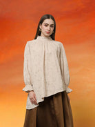 Woman wearing a light beige blouse with floral patterns by Kasa Heritage and brown pants against an orange gradient background