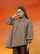Woman wearing a brown blouse with floral details by Kasa Heritage against an orange background