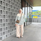 Woman in hijab wearing a green stripe shirt by Abame standing against a modern building with glass windows.