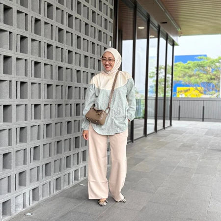 Woman in hijab wearing a green stripe shirt by Abame standing against a modern building with glass windows.