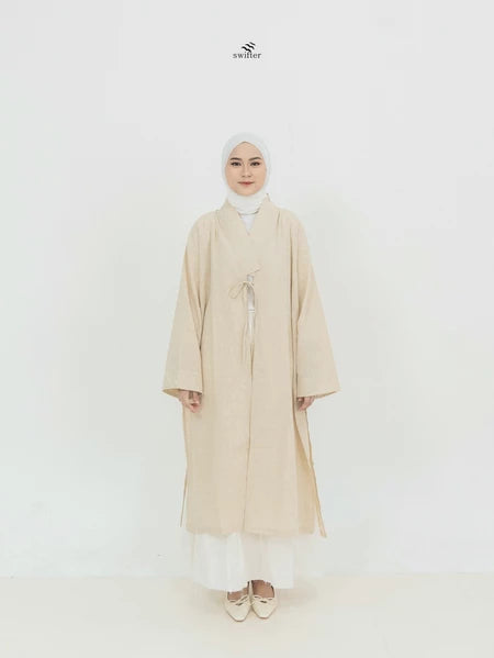 A woman modeling a beige Yuki Linen Outer kimono by Swifter with wide sleeves and a loose design, presented against a white background.