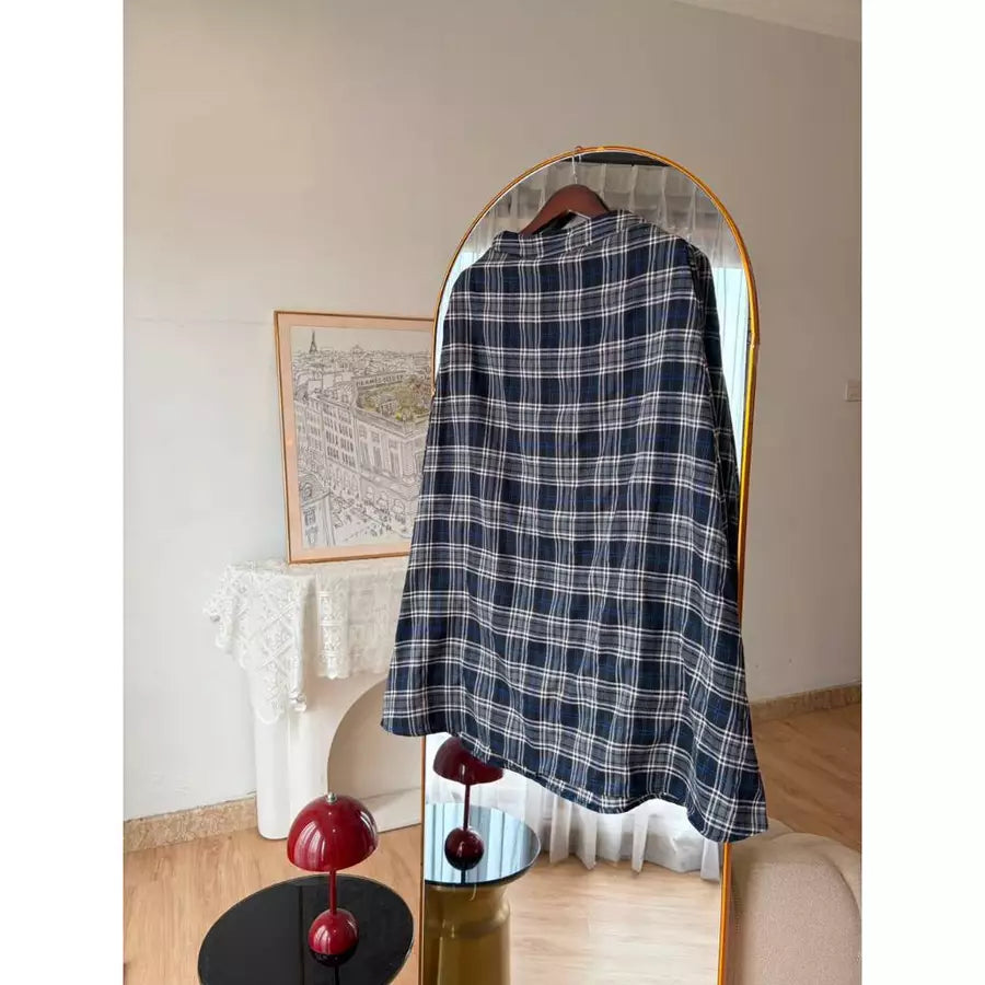 A navy blue and white plaid shirt by Haidee Orlin hanging on a wooden hanger in front of a gold-framed arched mirror, set in a styled room with a fireplace and decorative red mushroom lamps.