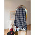 A navy blue and white plaid shirt by Haidee Orlin hanging on a wooden hanger in front of a gold-framed arched mirror, set in a styled room with a fireplace and decorative red mushroom lamps.