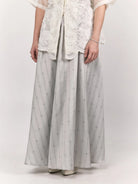 Person wearing a white embroidered top and light gray wide-leg patterned skirt by Studio Tui on a white background