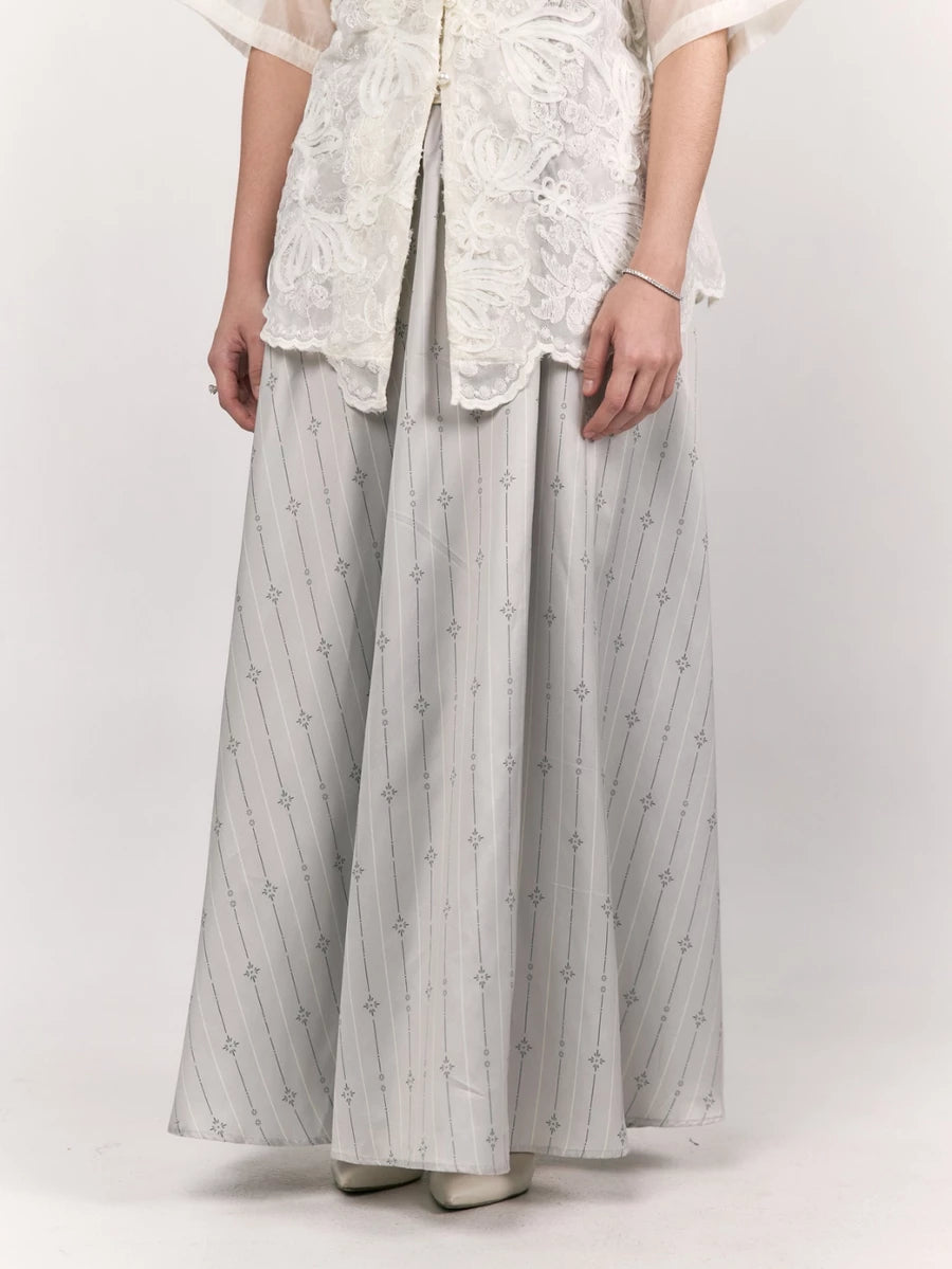 Person wearing a white embroidered top and light gray wide-leg patterned skirt by Studio Tui on a white background