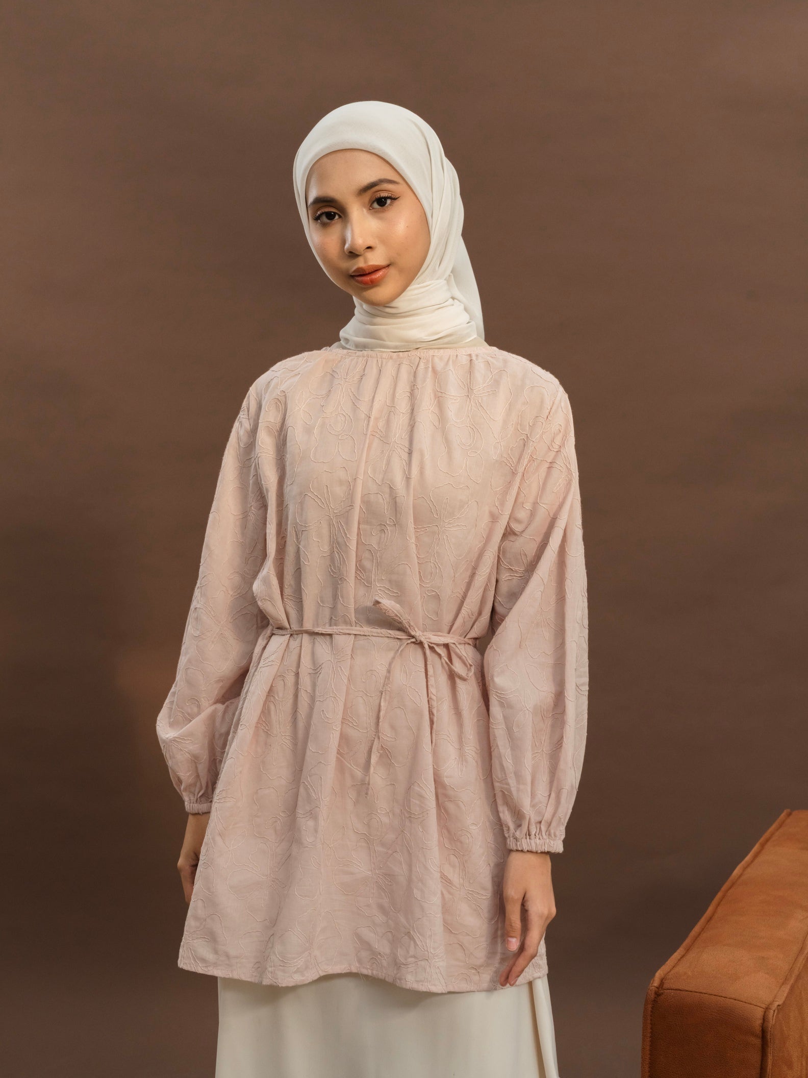 A woman wearing a pink long tunic with floral pattern, featuring tie details at the neckline and bishop sleeves with elastic cuffs from BWBYAZ.