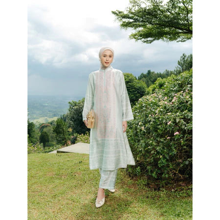 Woman in a light green outfit set of tunic and pants from Haidee Orlin standing in a scenic outdoor setting with trees and grass.