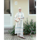 Woman in a ivory color and blue patterned traditional outfit by Haidee Orlin standing in front of a building with flowers.