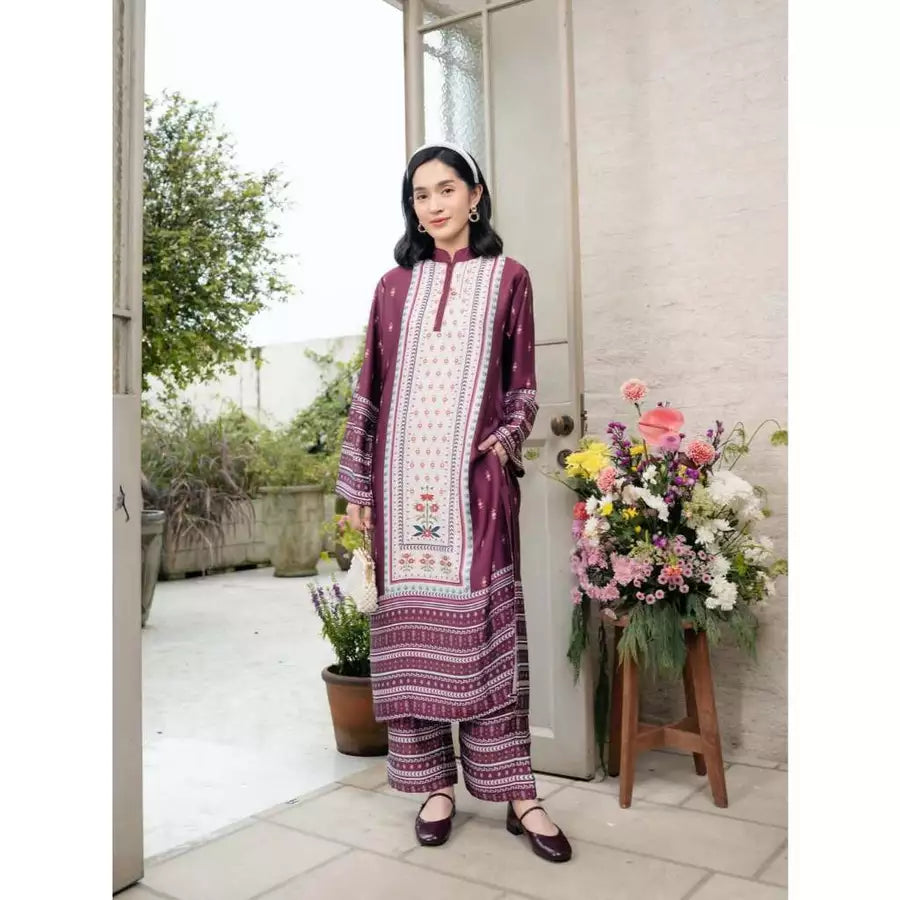 Woman in a maroon patterned traditional outfit by Haidee Orlin standing in a doorway with flowers and plants around.