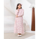 Young girl in a pink floral dress by Kasa Heritage standing in a room with a white wall and wooden lamp.