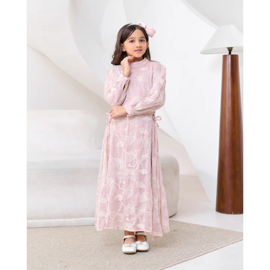 Young girl in a pink floral dress by Kasa Heritage standing in a room with a white wall and wooden lamp.