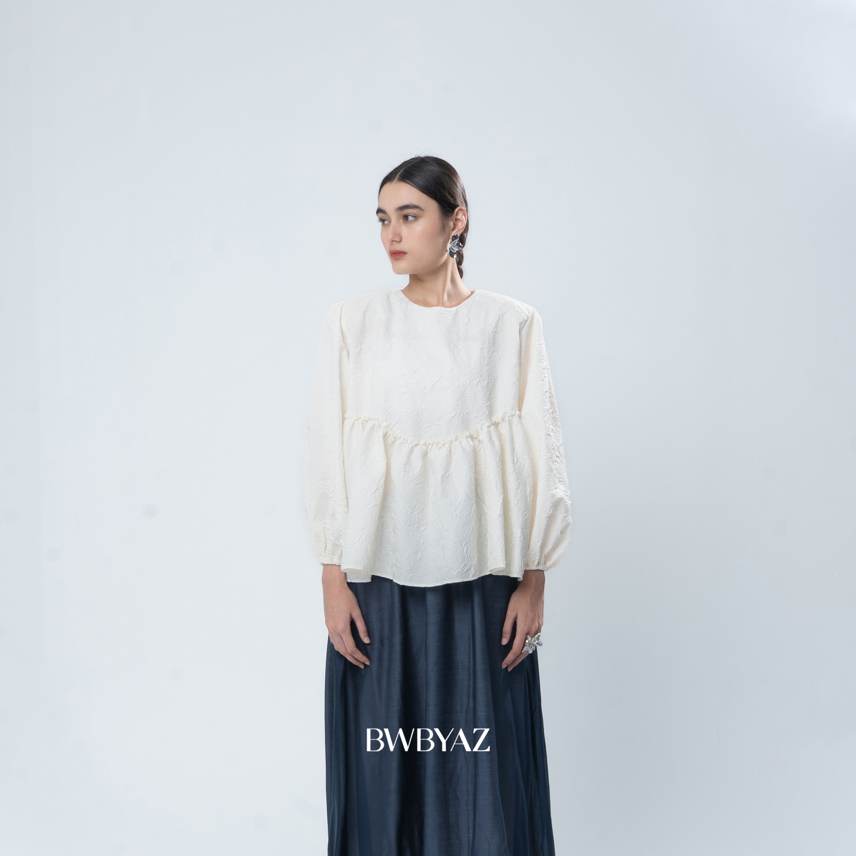 Person wearing a ivory white blouse and dark pants on a light gray background with 'BWBYAZ' branding.
