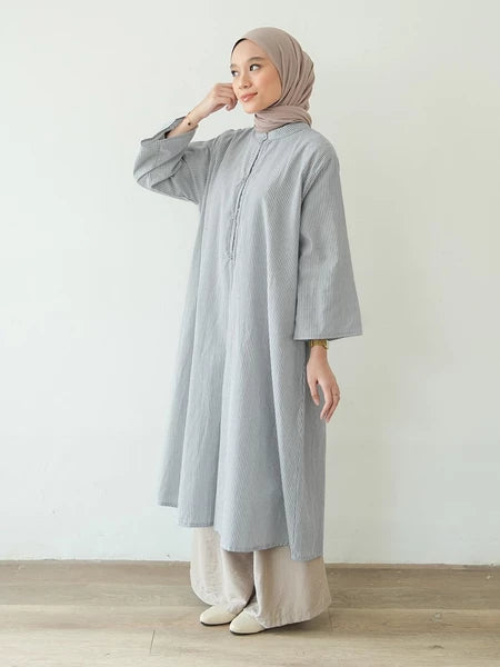 Woman wearing a light gray long-sleeve tunic by Mistyvori and beige pants with a beige hijab against a white background