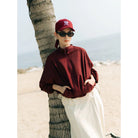 Person wearing a maroon track jacket by Haidee Orlin and cap.