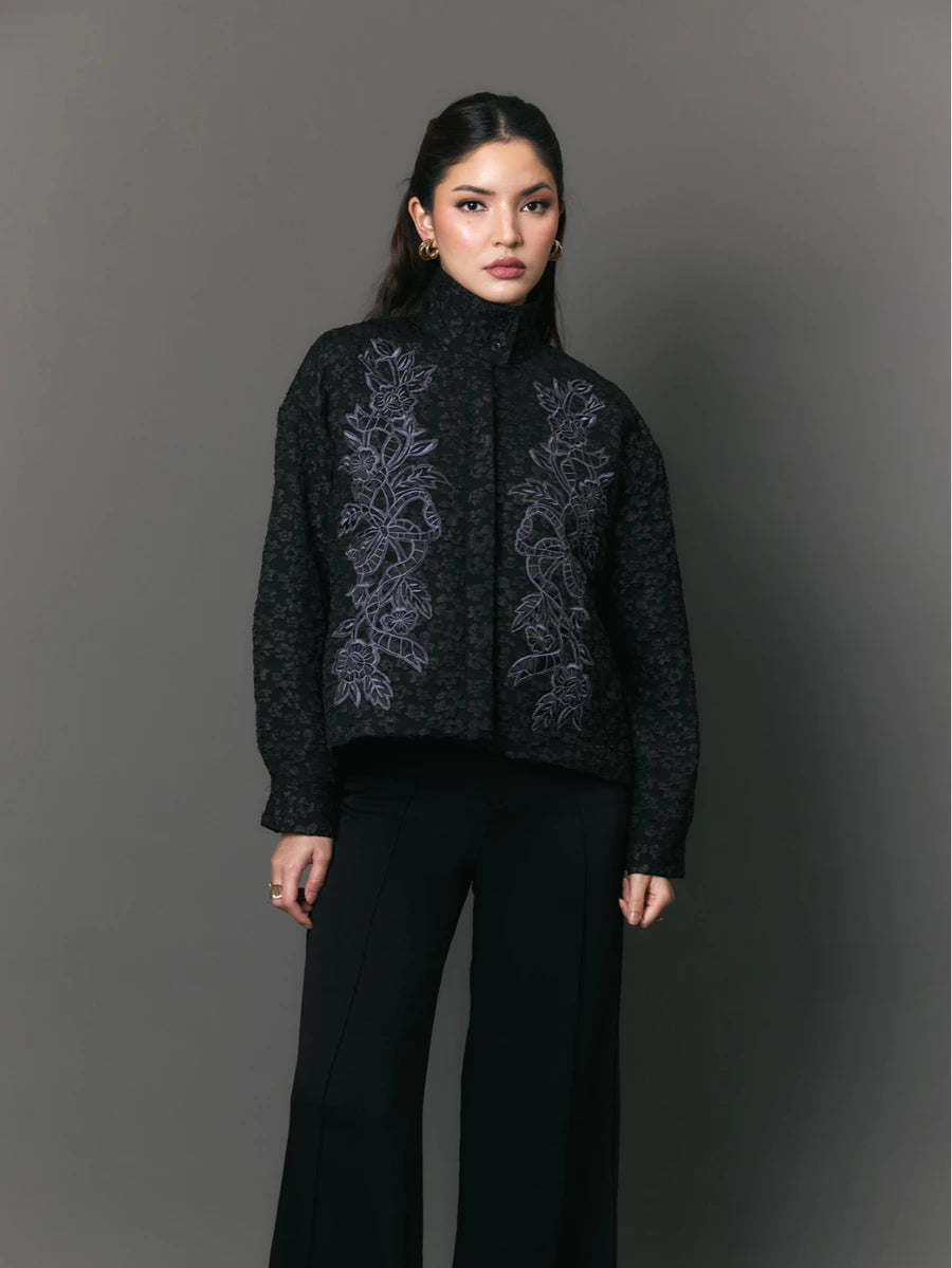Woman wearing a black jacket with floral embroidery by Studio Tui against a gray background