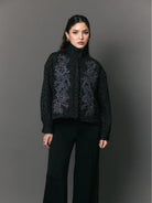 Woman wearing a black jacket with floral embroidery by Studio Tui against a gray background